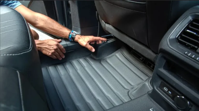 Close-up of a person installing a molded automotive floor mat in the rear passenger area of a vehicle interior.